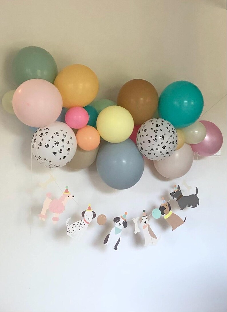 May include: A vibrant balloon display in pastel shades of pink, yellow, and blue. The arrangement includes paw print balloons and a dog-themed banner with party hats. Ideal for a dog-themed birthday celebration.