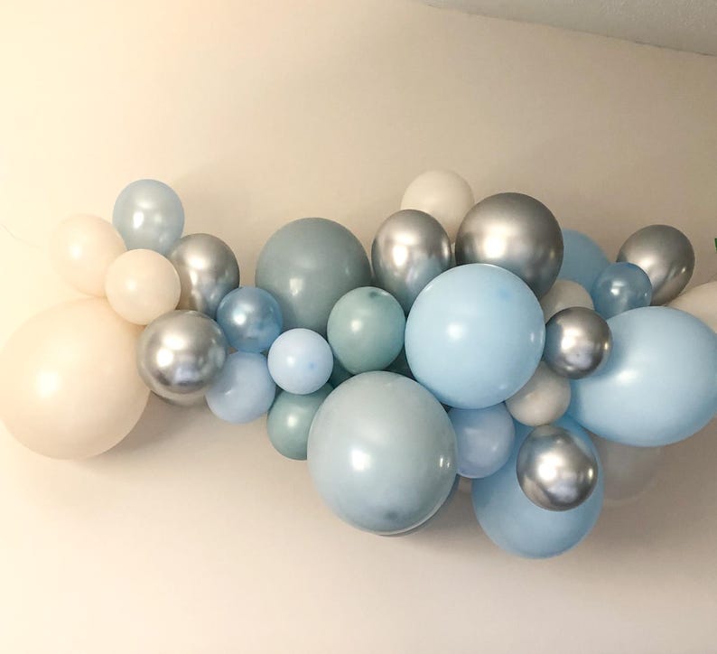 K&ouml;nnte beinhalten: Eine Ansammlung pastellfarbener Ballons in verschiedenen Gr&ouml;&szlig;en und Schattierungen von Blau, Silber und Creme. Die Ballons sind in einem Cluster angeordnet und bilden eine dekorative Darstellung. Mit matten und metallischen Oberfl&auml;chen.