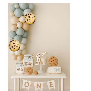 Peut inclure: Décoration de premier anniversaire avec une arche de ballons aux couleurs pastel. La table présente des décorations sur le thème des biscuits, dont un gâteau, des biscuits et des pots avec l'inscription "Milk". Une bannière indique "ONE".