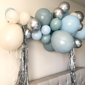 K&ouml;nnte beinhalten: Eine Ballongirlande in Wei&szlig;-, Silber- und Blaut&ouml;nen. Die Anordnung umfasst unterschiedlich gro&szlig;e Ballons, erg&auml;nzt durch silberne Fransen. Geeignet f&uuml;r eine Party oder Feier, die eine festliche Note zur Dekoration hinzuf&uuml;gt.