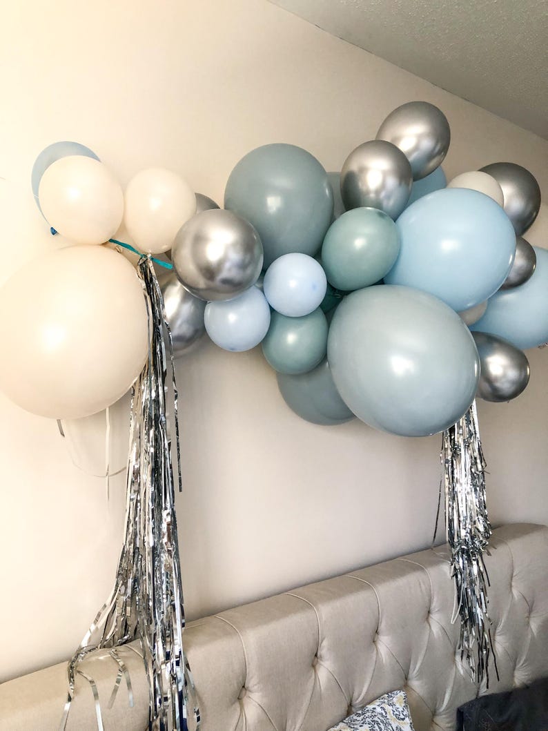 K&ouml;nnte beinhalten: Eine Ballongirlande in Wei&szlig;-, Silber- und Blaut&ouml;nen. Die Anordnung umfasst unterschiedlich gro&szlig;e Ballons, erg&auml;nzt durch silberne Fransen. Geeignet f&uuml;r eine Party oder Feier, die eine festliche Note zur Dekoration hinzuf&uuml;gt.