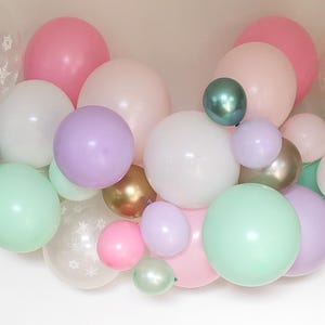 May include: A collection of pastel-colored balloons in various sizes. The balloons include shades of pink, white, green, purple, and gold. Some balloons are clear with snowflake patterns, creating a festive and celebratory atmosphere.