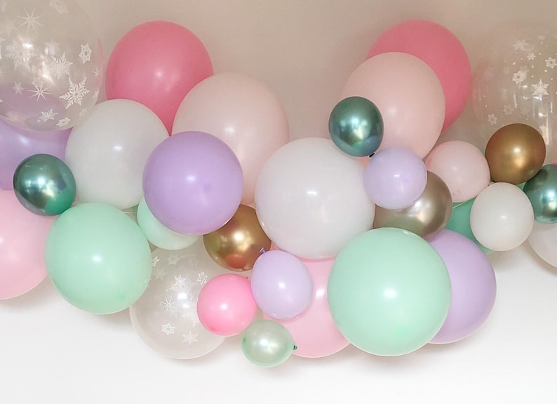 May include: A collection of pastel-colored balloons in various sizes. The balloons include shades of pink, white, green, purple, and gold. Some balloons are clear with snowflake patterns, creating a festive and celebratory atmosphere.