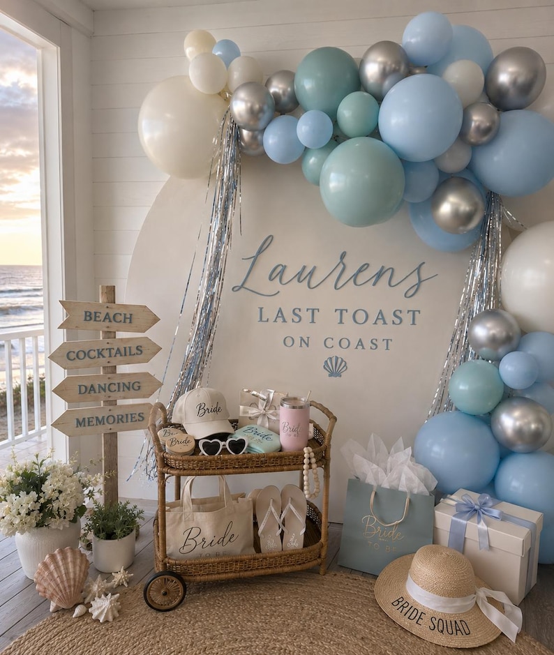 K&ouml;nnte beinhalten: Eine Strandparty-Dekoration mit einem Schild mit der Aufschrift &bdquo;Strand, Cocktails, Tanzen, Erinnerungen&ldquo;. Ein Wagen enth&auml;lt Accessoires zum Thema Braut, darunter ein Hut, eine Sonnenbrille und eine Tragetasche. Ballons in Blau- und Silbert&ouml;nen schm&uuml;cken den Hintergrund. Der Text &bdquo;Laurens Last Toast On Coast&ldquo; ist ebenfalls sichtbar.