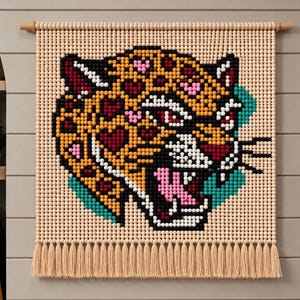 Könnte beinhalten: Ein Wandbehang aus hellen Holzperlen, die in einem Raster angeordnet sind und ein verpixeltes Leopardenkopf-Design bilden. Der Leopard ist gelb mit schwarzen Flecken, roten und rosafarbenen Herzmustern, weißen Zähnen und türkisfarbenen Akzenten, abgerundet mit einer Fransenborte.