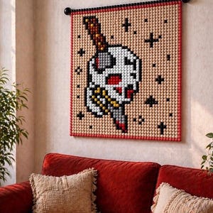 May include: A wall hanging featuring a skull pierced by a knife, created with small wooden beads. The skull is white with red accents, and the knife has a brown handle. The background is tan with black cross details, framed in red.