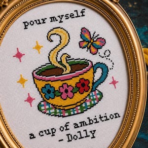 Op de afbeelding: Een kruissteekborduurwerk in een ovale gouden lijst met een gele theekop met blauwe, roze en rode bloemen, stoom, een kleurrijke vlinder en fonkelende sterren. De tekst luidt: pour myself a cup of ambition - Dolly.