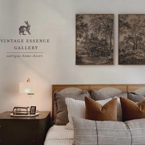 May include: A bedroom interior with a wooden headboard and a bed dressed in a gray and white striped duvet cover. Two framed black and white landscape prints hang above the headboard. A bedside table with a lamp and a small framed picture sits next to the bed. The text "Vintage Essence Gallery, antique home decor" is printed on the wall.