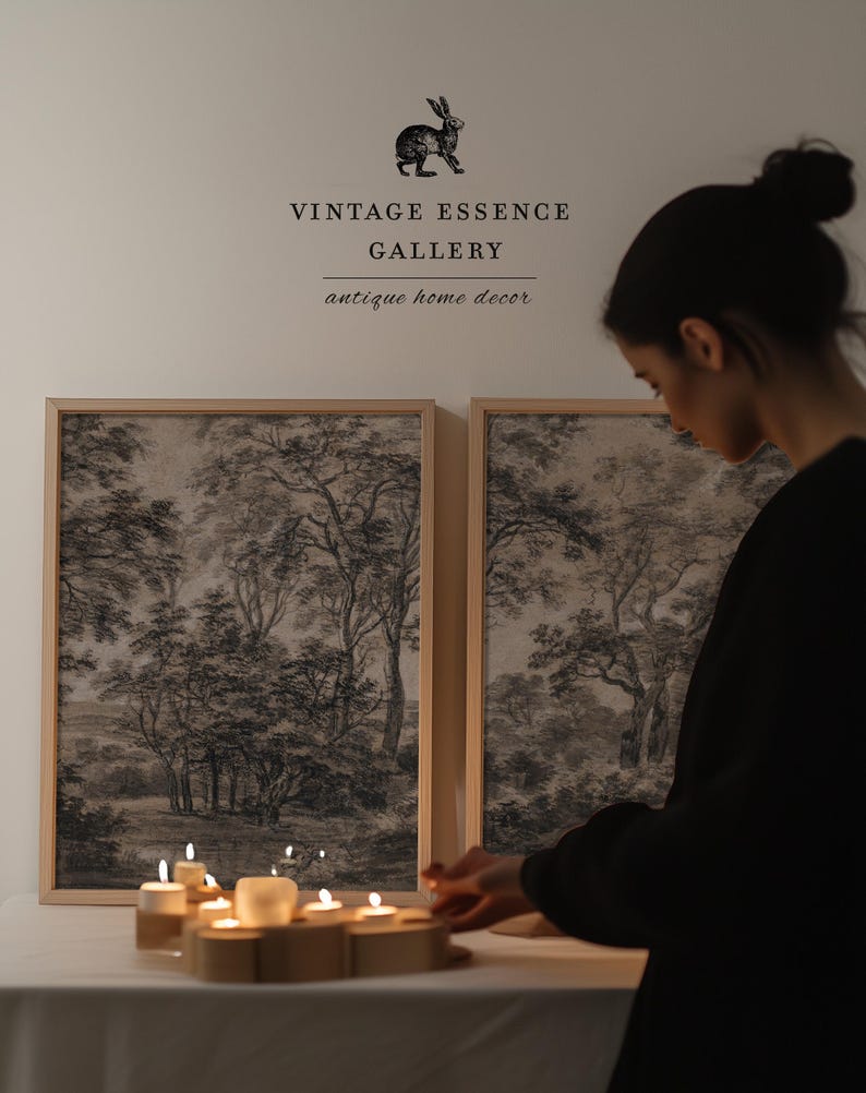 May include: Two framed black and white landscape prints of trees and a forest scene. A person is lighting candles on a table in front of the prints. The text above the prints reads "Vintage Essence Gallery antique home decor".