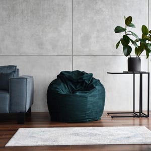 May include: A dark green bean bag chair in a modern living room setting with a grey concrete wall, a black side table, and a potted plant.