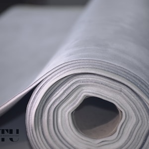 Puede incluir: Primer plano de una lámina de aislamiento de espuma gris texturizada enrollada. La espuma está enrollada apretadamente y los bordes son visibles. La espuma se utiliza para el aislamiento en edificios y otras estructuras.