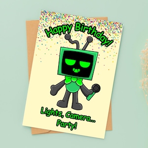 May include: Birthday card featuring a cartoon robot with a green screen head, holding a microphone. The card reads "Happy Birthday!" and "Lights, Camera... Party!" with colorful confetti. The card is on a brown envelope.