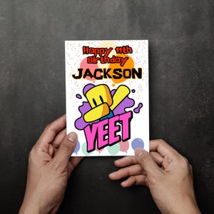 May include: A birthday card with the text "Happy 11th Birthday JACKSON" in orange and black. The card features a cartoon character and the word "YEET" in pink. Colorful confetti and balloons decorate the card.