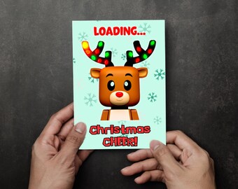 May include: A Christmas greeting card held by hands, featuring a cartoon reindeer with antlers adorned with colorful lights. The card has the words "LOADING..." and "Christmas CHEER!" on a light blue background with snowflakes.