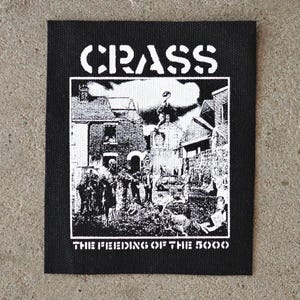 Puede incluir: Parche cuadrado negro con la palabra "CRASS" en letras blancas en la parte superior. Debajo, una ilustración en blanco y negro de una escena callejera con figuras. El texto "THE FEEDING OF THE 5000" está impreso en blanco en la parte inferior.