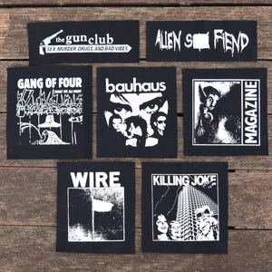 Puede incluir: Colección de parches en blanco y negro con logotipos de bandas y texto. Los parches incluyen "the gun club", "Alien Sex Fiend", "Gang of Four", "Bauhaus", "Magazine", "Wire" y "Killing Joke". Los parches son cuadrados y rectangulares.