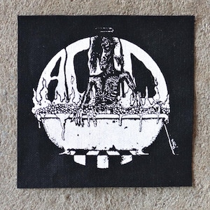 May include: Black square patch with a white graphic of a figure in a cauldron, surrounded by flames and the letters "A" and "L". The design is reminiscent of a vintage punk or metal band logo.