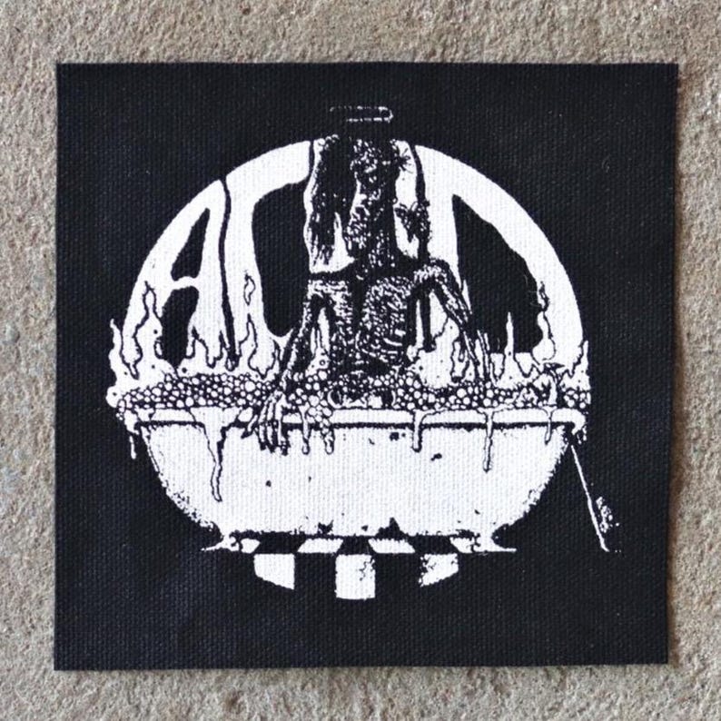 K&ouml;nnte beinhalten: Schwarz-wei&szlig;er Aufn&auml;her mit einer verst&ouml;renden Illustration einer Figur in einer Wanne, umgeben von Flammen. Die Buchstaben "AC" sind in einem Kreis zu sehen. Der Aufn&auml;her ist quadratisch und aus Stoff.