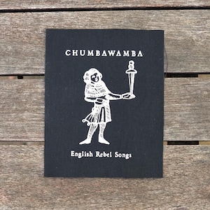 Puede incluir: Parche de tela negro con texto blanco y una ilustración blanca de una persona sosteniendo una espada. El texto dice "Chumbawamba English Rebel Songs."