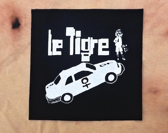May include: Black and white embroidered patch with the text "Le Tigre" and a cartoon image of a car and a person.