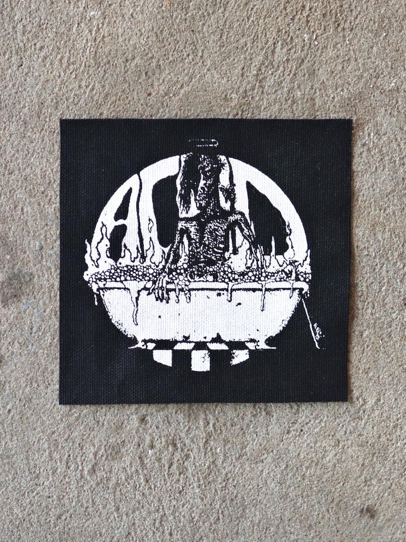 K&ouml;nnte beinhalten: Schwarzer quadratischer Aufn&auml;her mit einer wei&szlig;en Grafik einer Figur in einem Kessel, umgeben von Flammen und den Buchstaben "A" und "L". Das Design erinnert an ein Vintage-Punk- oder Metal-Band-Logo.