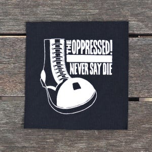 Peut inclure: Patch thermocollant noir et blanc avec une botte blanche et le texte "The Oppressed! Never Say Die."