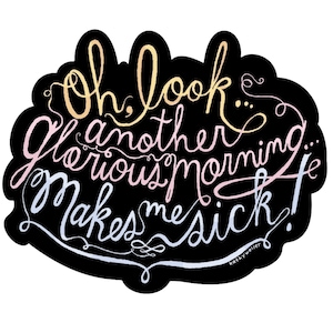 May include: A black sticker with the phrase "Oh, look another glorious morning... Makes me sick!" in a whimsical, handwritten style. The text is in shades of yellow, pink, and white, with the artist's signature at the bottom.