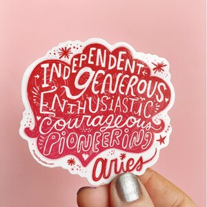 May include: Red and white sticker with the words "Independent, Generous, Enthusiastic, Courageous, Pioneering" and "Aries" in a stylised font. The sticker is in the shape of a cloud.
