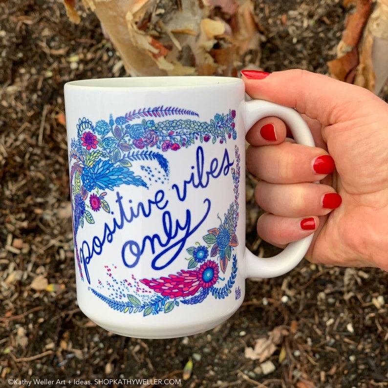 May include: White ceramic mug with a floral design and the text "positive vibes only" in blue and pink lettering.