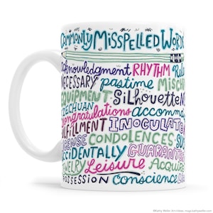 May include: White ceramic mug with a colorful word cloud design that reads "Commonly Misspelled Words". The words are in various colors, including pink, purple, green, and blue. The mug has a handle and a white background.