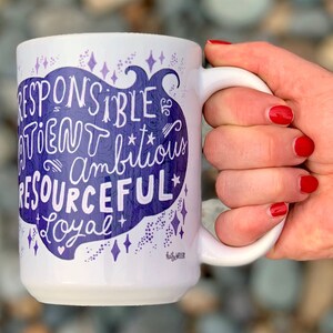 May include: White ceramic mug with a purple design that says "Responsible, Driven, Ambitious, Resourceful, Loyal" with stars and a heart. The mug is 15 ounces.