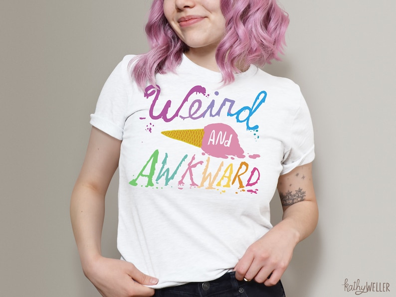May include: White t-shirt with a rainbow-colored graphic that says "Weird and Awkward" with a melting ice cream cone design.