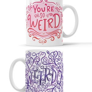 May include: Two white ceramic mugs with a whimsical design. The first mug features a pink and red watercolor design with the text "You're so WEIRD". The second mug features a purple watercolor design with the text "WEIRDO" in a swirling font.