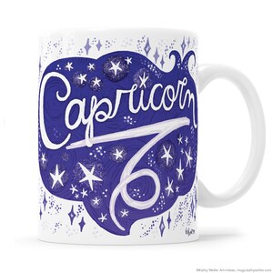 May include: White ceramic mug with a blue and white design featuring the zodiac sign Capricorn and the word "Capricorn" in a stylized font. The design is surrounded by white stars on a blue background.