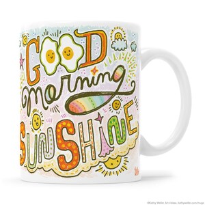 May include: White ceramic mug with a colorful design featuring the text "Good morning sunshine" with a rainbow, clouds, and suns.