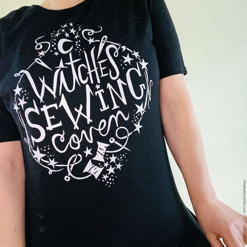 May include: Black t-shirt with a white graphic design of a circle with stars and the text "Witches Sewing Coven".