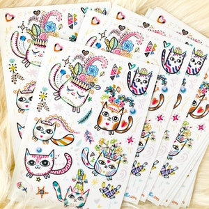 Peut inclure: Un ensemble de six autocollants color&eacute;s repr&eacute;sentant des chats fantaisistes avec des couronnes de fleurs et d'autres &eacute;l&eacute;ments d&eacute;coratifs. Les autocollants sont imprim&eacute;s sur du papier blanc et ont une finition brillante.