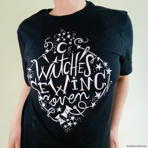 May include: Black t-shirt with a white graphic design that says "Witches Sewing Coven" with stars and other decorative elements.