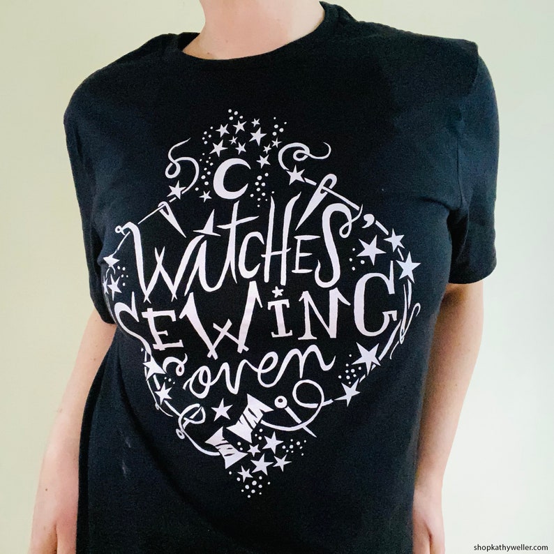 May include: Black t-shirt with a white graphic design that says "Witches Sewing Coven" with stars and other decorative elements.