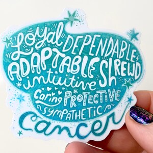 May include: A teal and white sticker with the word "Cancer" at the bottom. The sticker features the words "Loyal, Dependable, Adaptable, Shrewd, Intuitive, Caring, Protective, Sympathetic" in a whimsical font, with star and heart accents.