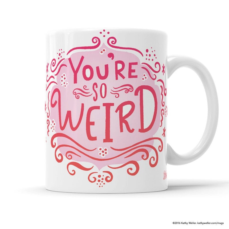 May include: White ceramic coffee mug with a pink and red design that says "You're so weird" in a whimsical font. The design is surrounded by swirls and dots.