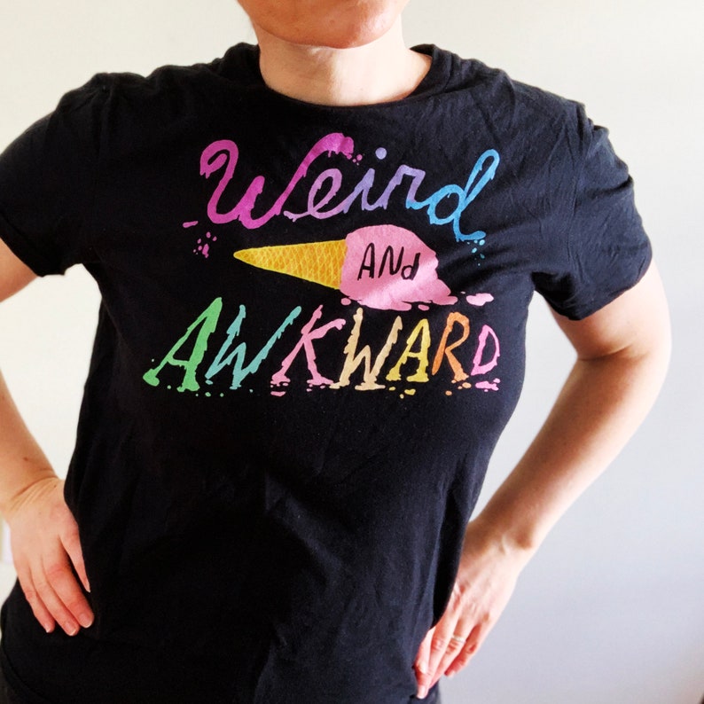 May include: Black t-shirt with a colorful graphic of an ice cream cone and the text "Weird and Awkward".