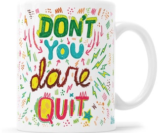 Könnte beinhalten: Eine weiße Keramiktasse mit einem bunten Design, auf dem "Don't you dare quit" steht. Das Design zeigt eine Vielzahl von Farben, darunter Grün, Gelb, Rot, Blau und Braun. Die Tasse ist mit verschiedenen Kritzeleien verziert, darunter Blitze, Sterne und Punkte.