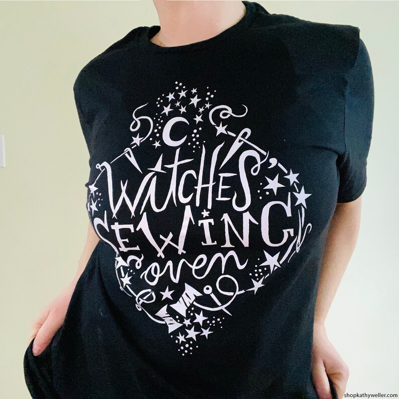 May include: Black t-shirt with a white graphic design that says "Witches Brewing Coven" with stars and other witchy symbols.