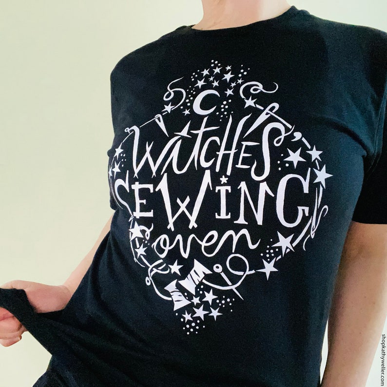 May include: Black t-shirt with a white graphic design that says "Witches Sew In" with a crescent moon, stars, and a needle and thread design.