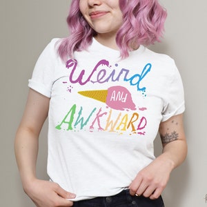 May include: White t-shirt with a rainbow-colored graphic that says "Weird and Awkward" with a melting ice cream cone design.