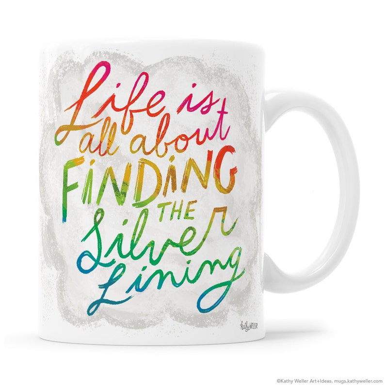 May include: White ceramic mug with a rainbow-colored design that says "Life is all about finding the silver lining".