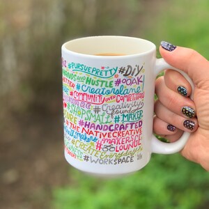 May include: White ceramic mug with a colourful design featuring the words "#PURSUE PRETTY #DIY #HANDS AND HUSTLE #OOAK #CREATORSLANE #COMMUNITYOVER COMPETITION #SHARE #CREATIVITY #SHOPSMALL #MAKER #SURE #HANDCRAFTED #THE NATIVECREATIVE #MAKERS #MAKERS #CREATE #EVERYDAY #BUSINESS #WORKSPACE #BOLOUNGE".