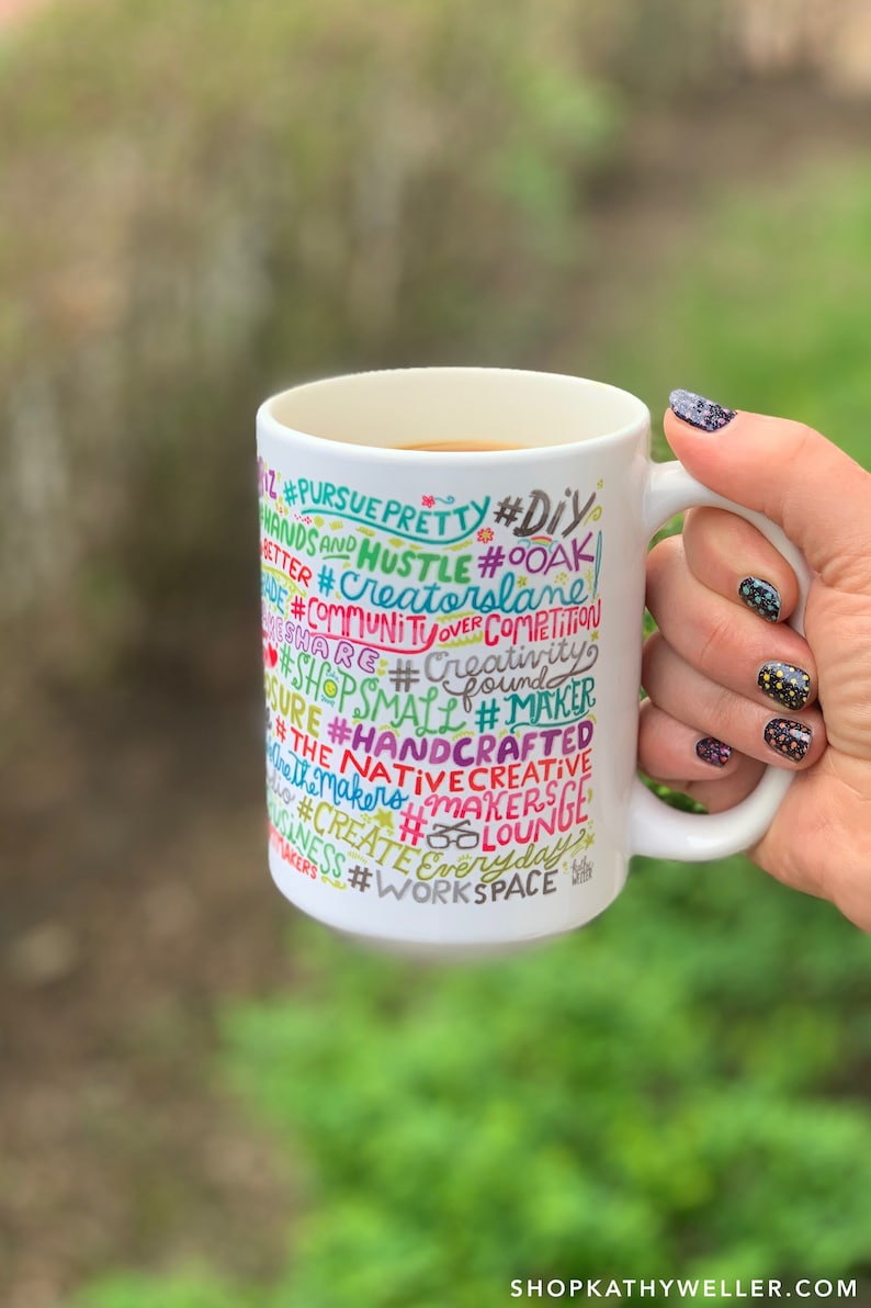 May include: White ceramic mug with a colourful design featuring the words "#PURSUE PRETTY #DIY #HANDS AND HUSTLE #OOAK #CREATORSLANE #COMMUNITYOVER COMPETITION #SHARE #CREATIVITY #SHOPSMALL #MAKER #SURE #HANDCRAFTED #THE NATIVECREATIVE #MAKERS #MAKERS #CREATE #EVERYDAY #BUSINESS #WORKSPACE #BOLOUNGE".