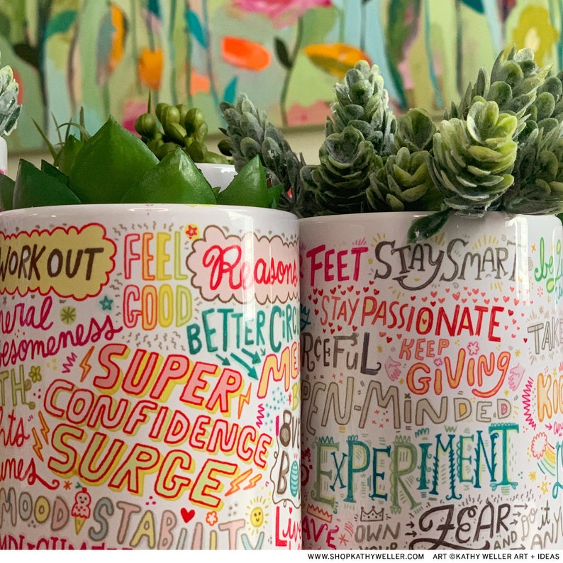 May include: Two white ceramic mugs with colorful handwritten inspirational words and phrases like "Workout," "Super Confidence Surge," and "Stay Passionate." The mugs are filled with green artificial plants.